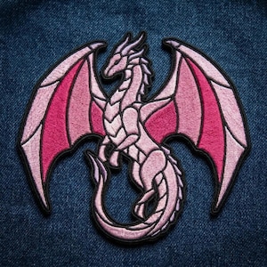 May include: An embroidered patch featuring a dragon in shades of light pink and magenta. The dragon is depicted with its wings spread wide, a long curved tail, and a detailed body structure, all outlined with a thick black border for definition.