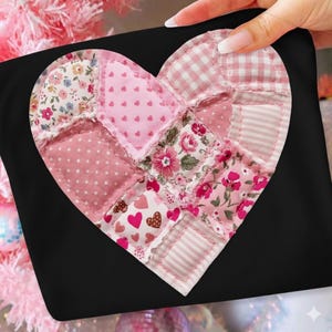 Pode incluir: Uma almofada preta com um design em forma de coração. O coração é um patchwork de vários tecidos rosa, incluindo padrões florais, de bolinhas e listrados. O design do coração está centrado na almofada.