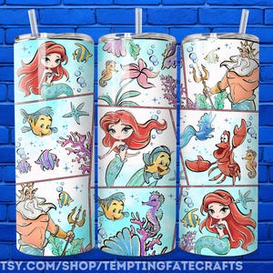 A collection of three colorful tumblers featuring illustrations of mermaids and marine life, such as fish and sea creatures, against a blue brick wall background.