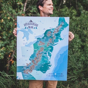 May include: A person holds a blue and green map of the Appalachian Trail. The map shows the trail's route through the eastern United States. The text on the map reads "Appalachian Trail" and "It's all about the journey."