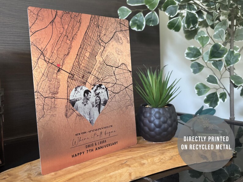 May include: A copper-colored metal print with a map of New York City. A heart-shaped photo of a couple is in the center of the map. The text "Where it all began..." is written below the photo. The text "David & Laura" and "Happy 7th Anniversary" is written below the map. The print is directly printed on recycled metal.