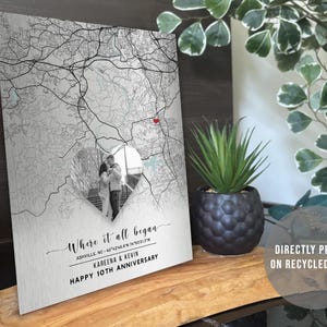 May include: A metal print featuring a map design with a heart-shaped cutout showcasing a couple's photo. The text reads "Where it all began" and "Happy 10th Anniversary." The print is directly printed on recycled metal.
