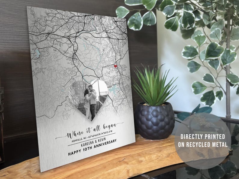 May include: A metal print featuring a map design with a heart-shaped cutout showcasing a couple's photo. The text reads "Where it all began" and "Happy 10th Anniversary." The print is directly printed on recycled metal.