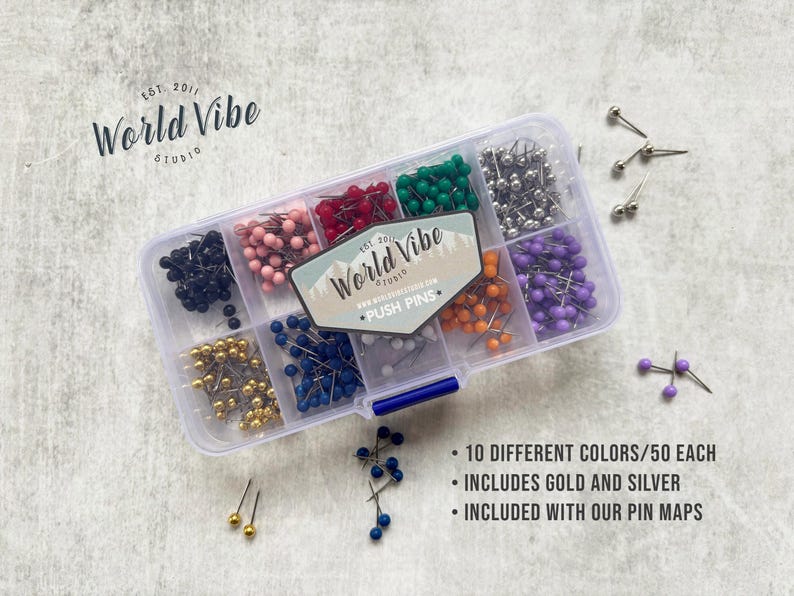 May include: A clear plastic container filled with 10 different colors of push pins, each color has 50 pins. The container has a label that says "World Vibe" and "Push Pins". The container is sitting on a white surface.  The text on the label reads: "World Vibe" and "Push Pins".