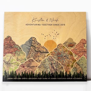 May include: A wooden sign with a map design featuring mountains and a sunset. The text "Kristen & Nick Adventuring Together Since 2015" is printed on the sign. The names of cities and locations are listed at the bottom of the sign.