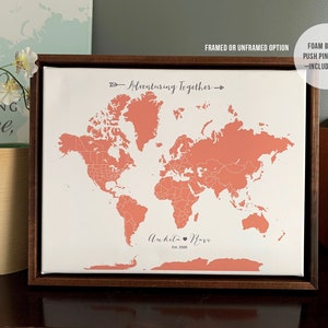 May include: A framed world map with a coral pink outline of the continents. The map is on a white background with the text "Adventuring Together" and "Ankita Ravi Est. 2023" printed below the map. The frame is a dark brown wood.