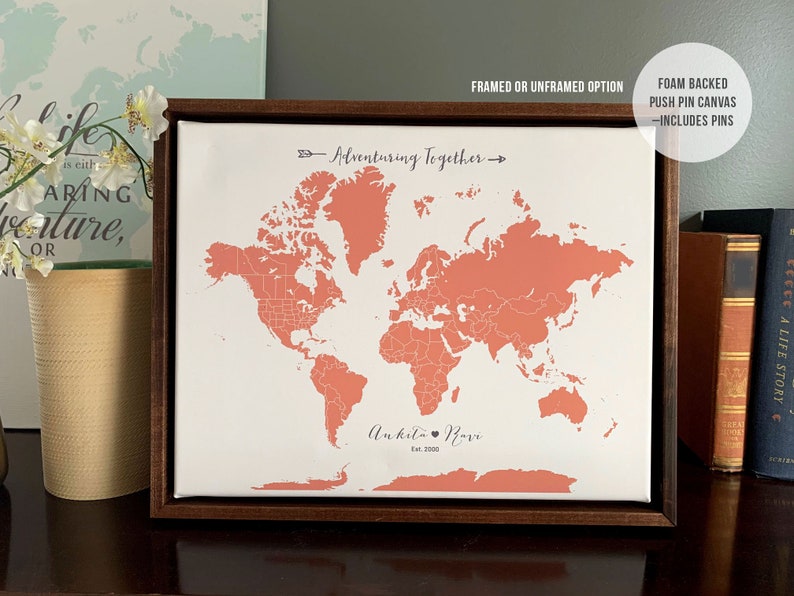 May include: A framed world map with a coral pink outline of the continents. The map is on a white background with the text "Adventuring Together" and "Ankita Ravi Est. 2023" printed below the map. The frame is a dark brown wood.
