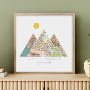 May include: A framed print with a mountain range made of vintage maps. The mountains are surrounded by a white background with a yellow sun at the top. The text "PAPA. THANK YOU FOR A LIFETIME OF ADVENTURES. Your kiddos" is at the bottom of the print.