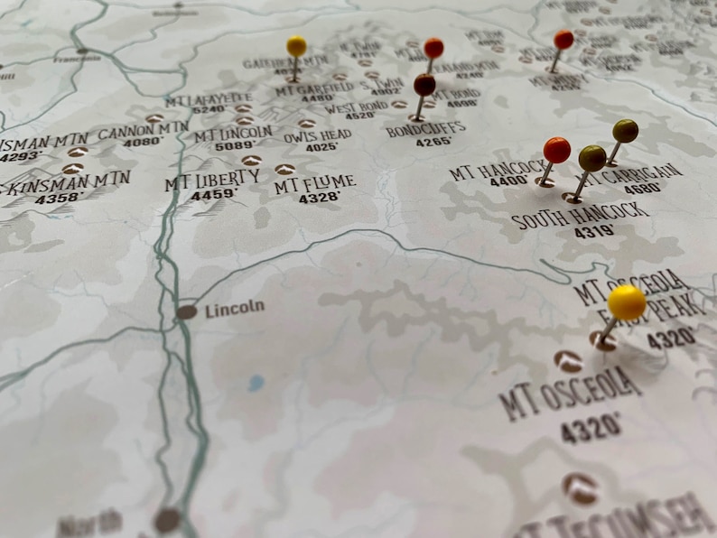 May include: A close-up of a map with push pins marking various locations. The map is printed on white paper with brown text and lines. The push pins are yellow, red, and green.