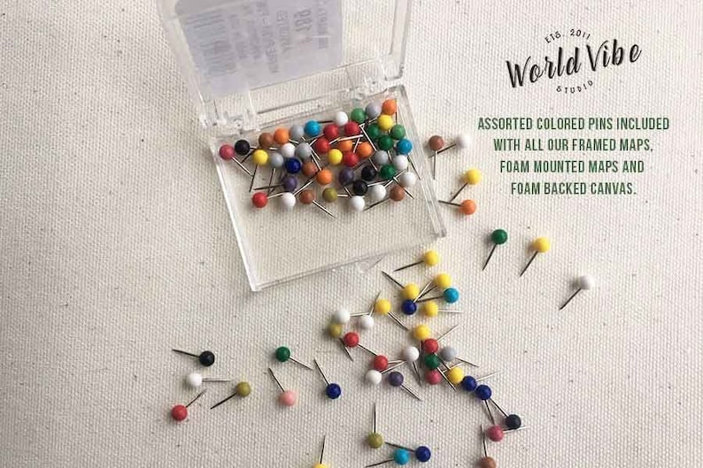 May include: A clear plastic container filled with colorful push pins. The container is open and the pins are scattered on a white canvas background. The text "World Vibe Studio" is printed on the container. The text "Assorted colored pins included with all our framed maps, foam mounted maps and foam backed canvas." is printed below the container.