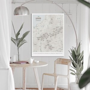 May include: A white framed map print with the title "4000 Footers" and a gray and white map of mountains and towns. The text "It is not the mountain we conquer but ourselves" is printed below the map.