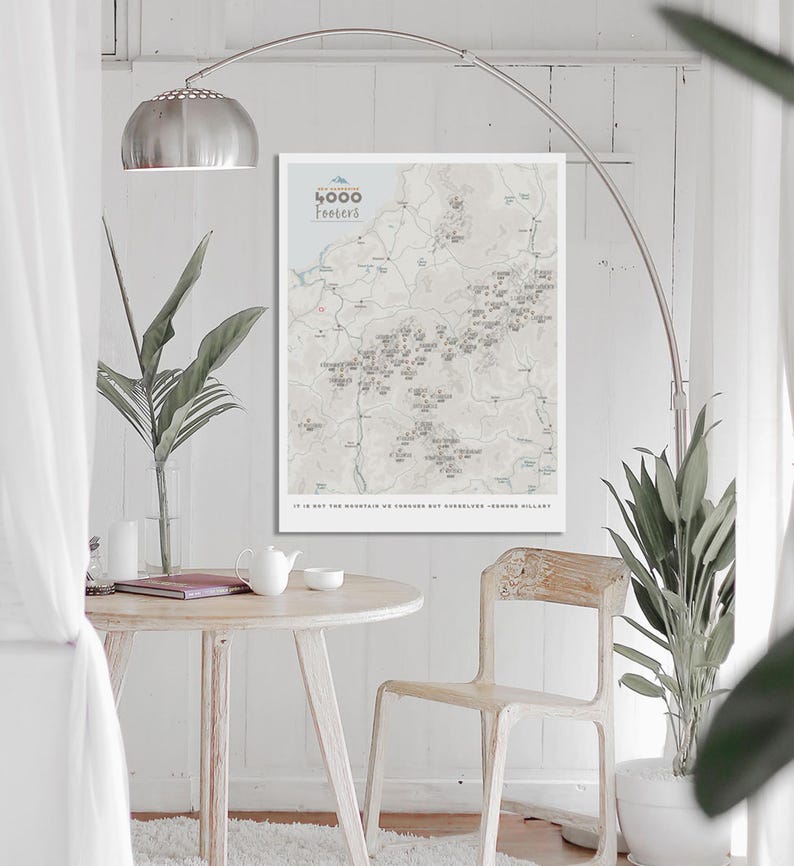 May include: A white framed map print with the title "4000 Footers" and a gray and white map of mountains and towns. The text "It is not the mountain we conquer but ourselves" is printed below the map.
