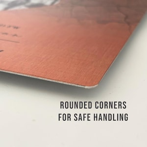 May include: Close-up of the corner of a red-brown metal sign with rounded edges. The text "ROUNDED CORNERS FOR SAFE HANDLING" is printed in black below the sign.