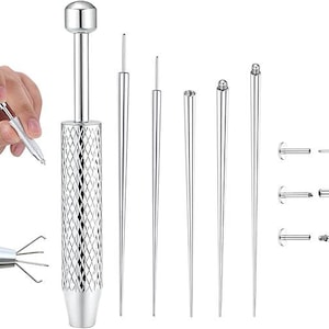 Puede incluir: Un juego de herramientas de perforación de color plateado. El juego incluye un mango grande y texturizado con una parte superior redondeada, varias herramientas cónicas y pequeñas joyas tipo barra. Una mano sostiene una herramienta pequeña.