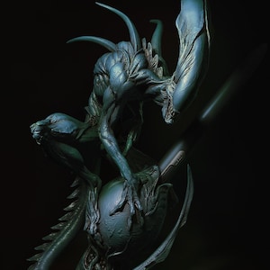 Può includere: Scultura dettagliata color teal di una creatura aliena con una lunga coda, punte e una grande testa. La creatura è posizionata sopra un oggetto scuro a forma di uovo. La scultura ha una superficie strutturata su sfondo nero.