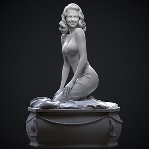 May include: A grayscale sculpture of a woman kneeling on a decorative base. The woman has wavy hair and is wearing a dress with a lace bodice. The base is rectangular with rope and tassel details.