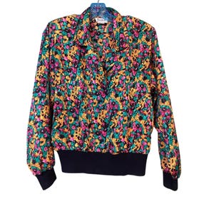 May include: A vintage floral print jacket with a black ribbed hem and cuffs. The jacket features a vibrant pattern of pink, yellow, green, and black flowers on a colorful background. The jacket has a collared neckline and long sleeves.