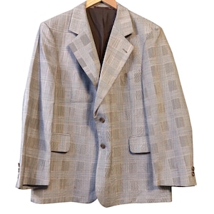 May include: A light gray blazer with a plaid pattern. The blazer has a notched lapel, two front pockets, and brown buttons. The interior lining is a dark brown color. The blazer is hanging on a wooden hanger.