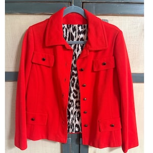 May include: A bright red jacket with a collared neckline and four front pockets. The jacket features black buttons and a striking leopard print lining. The jacket is hanging on a blue hanger.