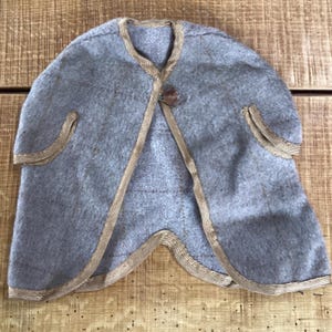 May include: A gray cape with gold trim and a single button closure. The cape has a rounded shape with decorative gold trim along the edges and around the button. The garment appears to be made of a soft, felt-like material.