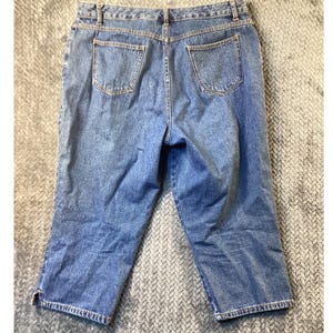 May include: Light blue denim capri pants with two back pockets and a button and zipper closure. The capris have a classic five-pocket design and are made of a durable denim fabric. The pants are a mid-rise style and have a relaxed fit.
