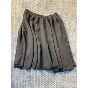 May include: A dark gray, knee-length skirt with a flowing, flared design. The skirt has a gathered waistband and a soft, silky texture. The fabric drapes in soft folds, creating a flattering silhouette. The skirt is suitable for various occasions.