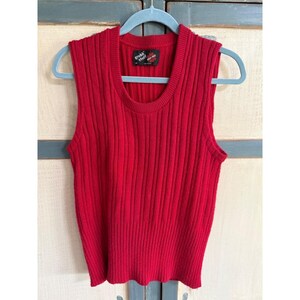 May include: A sleeveless, ribbed knit top in a vibrant red hue. The top features a crew neck and a straight hemline. A small tag with text is visible near the neckline. The garment is displayed on a blue hanger.
