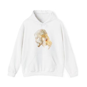 May include: White hoodie with a watercolour illustration of a man with long hair and a beard. The image is positioned on the front, above the pocket. The artwork has a soft, golden colour palette.