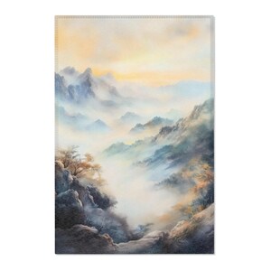 May include: A rectangular wall art print depicting a misty mountain landscape. The artwork features layers of blue and gray mountains, with a soft, ethereal quality. The sky transitions from yellow to a pale blue.
