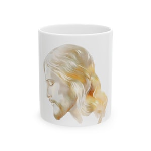 May include: White ceramic mug with a side profile portrait of a person with long, flowing, light brown hair and a beard. The portrait has a soft, watercolour-like appearance, with subtle shading and highlights.