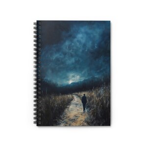 Puede incluir: Cuaderno de espiral con pintura de paisaje. La imagen muestra a una persona caminando por un camino hacia montañas bajo un cielo azul oscuro y tormentoso. La obra de arte en la portada del cuaderno evoca una sensación de misterio e introspección.