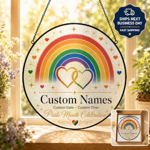 Puede incluir: Un atrapasoles circular de vidrio con un arcoíris vibrante sobre dos corazones entrelazados. El diseño incluye el texto Custom Names, Custom Date, Custom Time y Pride Month Celebration, decorado con pequeñas estrellas y corazones.