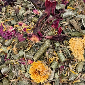 May include: Close-up of a mix of dried herbs and flowers. The blend includes green, brown, yellow, and purple elements. Visible components include dried flower petals, stems, and small, cylindrical pellets, suggesting a natural product.