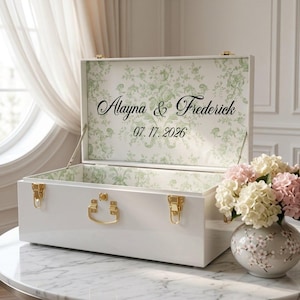 May include: A white rectangular keepsake box with gold-toned metal latches and a handle. The interior lid features a green floral damask pattern with the black printed text Alayna & Frederick and the date 07.17.2026 in a script font.