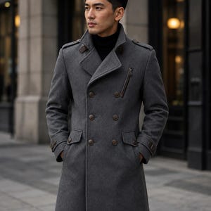 May include: A charcoal gray double-breasted wool-blend coat featuring a high collar, epaulets on the shoulders, and brown buttons. The coat includes two side flap pockets, a zippered chest pocket, and adjustable buttoned straps on the sleeve cuffs.