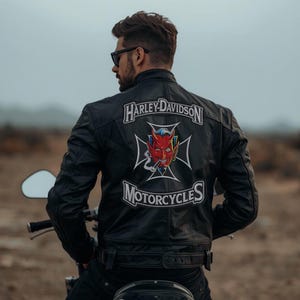 Puede incluir: Chaqueta de moto de cuero negro con el logotipo de Harley-Davidson y un gráfico de diablo rojo en la espalda. La chaqueta presenta un estilo motero clásico con cremallera frontal y un ajuste entallado. También es visible la palabra "MOTORCYCLES".