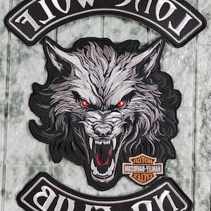 Op de afbeelding: Een zwart-wit geborduurde patch met een grommende wolf met rode ogen. De patch bevat gebogen banners met de tekst "Lone Wolf" en "No Crab". Er is ook een Harley-Davidson-logo aanwezig.