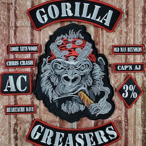 May include: A collection of embroidered patches with a biker theme. The central patch features a gorilla with a red bandana smoking a cigar. Other patches include text like "GORILLA", "GREASERS", and names. The patches are black, white, and red.