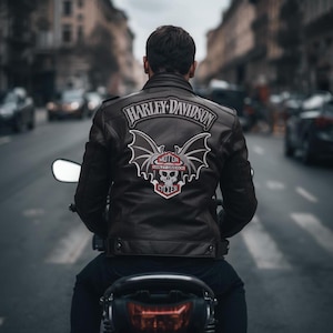 Puede incluir: Una chaqueta de cuero negra Harley-Davidson con un gran emblema en la espalda, usada por una persona en una motocicleta. El emblema presenta una calavera, alas y el logotipo de Harley-Davidson, con un fondo urbano.