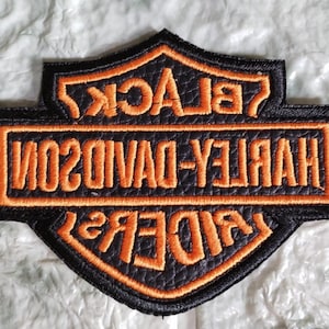 Puede incluir: Parche bordado negro y naranja con las palabras "HARLEY-DAVIDSON" y "BLACK RIDERS" en un diseño de escudo. El parche es negro con costuras naranjas.