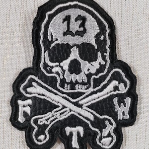 May include: Black and white embroidered patch featuring a skull with the number 13, crossed bones, and the letters F, T, and W. The patch has a black background with white stitching.