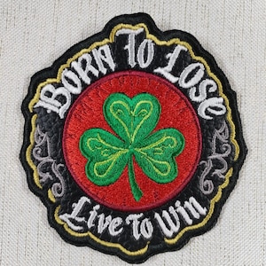 Puede incluir: Parche bordado con borde negro y el texto "BORN TO LOSE, LIVE TO WIN" en blanco. El parche presenta un círculo rojo con un trébol verde en el centro. El parche tiene un diseño decorativo en oro, gris y negro.