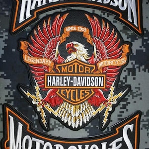 Puede incluir: Parche bordado de Harley-Davidson con un águila estilizada con alas rojas y blancas, una pancarta que dice "Legendary Motorcycles" y el texto "Since 1903". El parche es negro, naranja y blanco, con un fondo de camuflaje.
