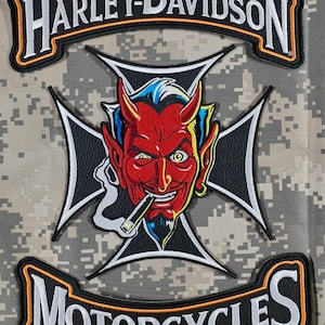 Puede incluir: Un parche de Harley-Davidson con un diablo rojo fumando un cigarro, sobre una cruz negra y blanca. Las palabras "HARLEY-DAVIDSON" y "MOTORCYCLES" están arqueadas arriba y abajo de la imagen central, delineadas en naranja y blanco.