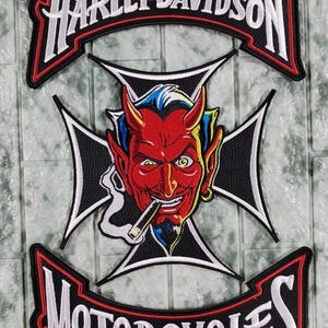 Puede incluir: Parche bordado con el logotipo de Harley-Davidson sobre un diablo fumando un cigarro, sobre una cruz en blanco y negro. La palabra "MOTORCYCLES" está debajo, todo con detalles en blanco y rojo.