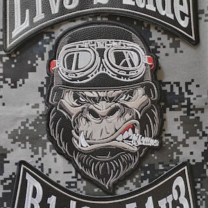 Puede incluir: Parche bordado con un gorila con gafas y casco, con el texto "L1v3 2 Ride" y "R1d3 2 L1v3". El parche es negro, blanco y gris, sobre un fondo de camuflaje.
