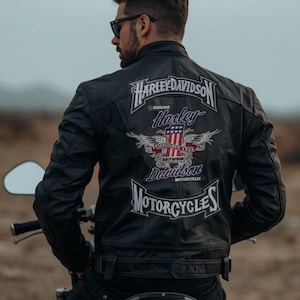 Puede incluir: Chaqueta de moto de cuero negro con parches de Harley-Davidson en la espalda. Los parches muestran el nombre de Harley-Davidson, alas y la bandera estadounidense. La chaqueta tiene un estilo motero clásico.