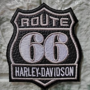 Puede incluir: Parche negro y gris de Route 66 Harley-Davidson. El parche presenta las palabras "ROUTE" y "66" en gris claro, con "HARLEY-DAVIDSON" en una pancarta rectangular en la parte inferior. El parche tiene una apariencia texturizada.