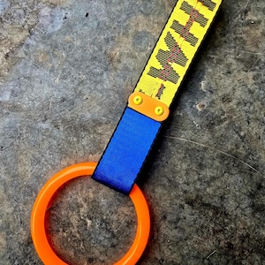 Puede incluir: Una correa amarilla y negra con el texto "KH" en negro, conectada a una correa azul y un anillo naranja. La correa se asegura con dos tornillos naranjas. El anillo es de color naranja brillante.