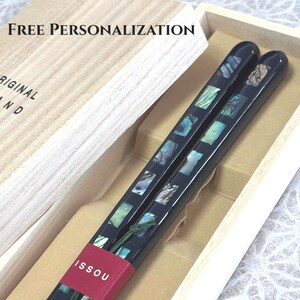 May include: A pair of black chopsticks with inlaid iridescent shell squares, held together by a red paper band labelled ISSOU. The chopsticks are presented in a light-coloured wooden box with the text FREE PERSONALIZATION and ORIGINAL printed.
